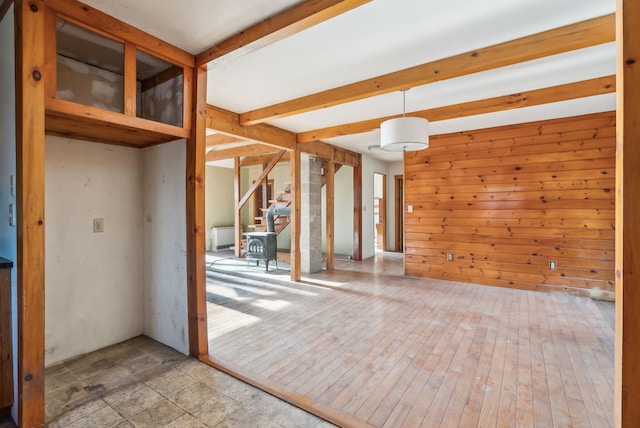 spare room featuring wood walls, a wood stove, and beam ceiling