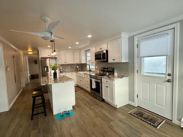 kitchen featuring a center island, crown molding, light stone countertops, white cabinetry, and stainless steel appliances