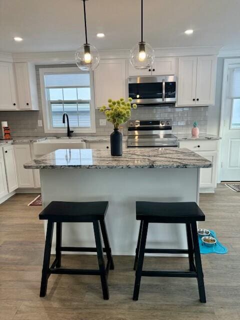 kitchen featuring white cabinetry, stainless steel appliances, light hardwood / wood-style flooring, decorative light fixtures, and a kitchen island