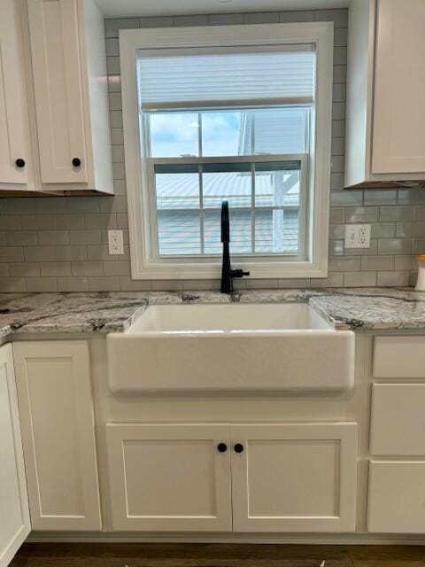 room details featuring decorative backsplash, light stone counters, white cabinetry, and sink