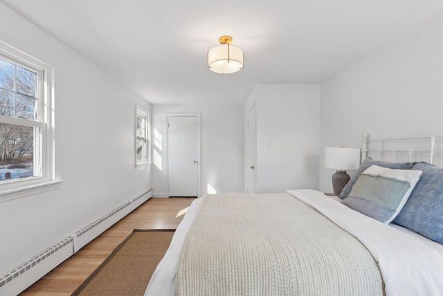 bedroom with baseboard heating, light hardwood / wood-style floors, and multiple windows