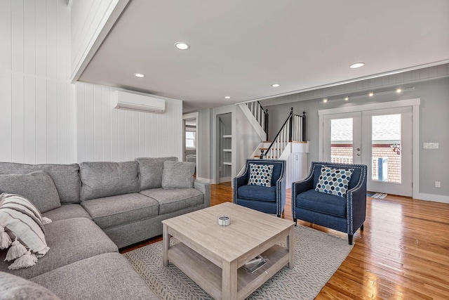 living room with a wall mounted air conditioner, wood-type flooring, french doors, and wooden walls