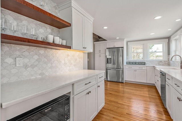 kitchen with appliances with stainless steel finishes, light wood-type flooring, white cabinetry, and backsplash