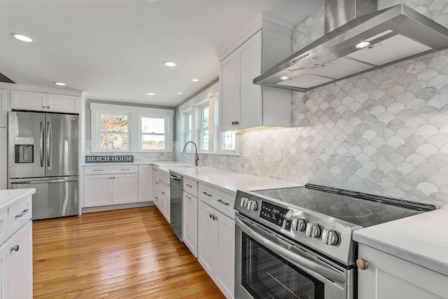 kitchen featuring white cabinets, light wood-type flooring, wall chimney range hood, and appliances with stainless steel finishes