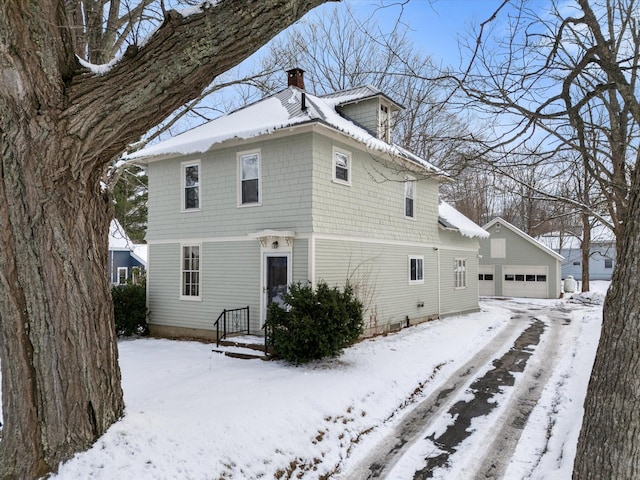 snow covered house featuring a garage and an outdoor structure