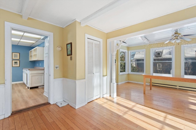 interior space featuring light wood-type flooring, ceiling fan, crown molding, a baseboard radiator, and beamed ceiling