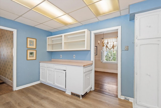 kitchen featuring white cabinets, a paneled ceiling, an inviting chandelier, and light hardwood / wood-style flooring