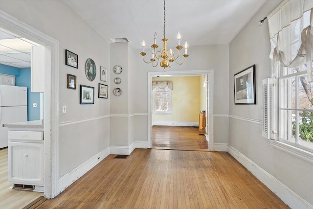 unfurnished dining area with light wood-type flooring and a chandelier