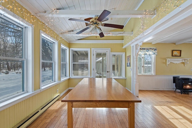 unfurnished sunroom with a wood stove, ceiling fan, a baseboard radiator, lofted ceiling with beams, and wood ceiling