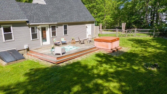 rear view of property featuring a wooden deck, a yard, and a hot tub