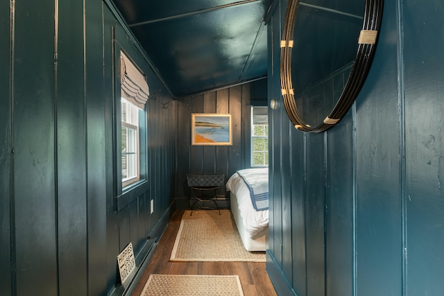 bedroom with dark hardwood / wood-style floors, wood walls, and lofted ceiling