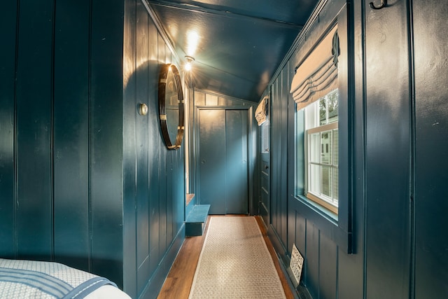 hall with hardwood / wood-style flooring, wood walls, and lofted ceiling