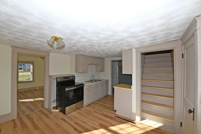 kitchen with light wood-type flooring, a textured ceiling, sink, and stainless steel electric range