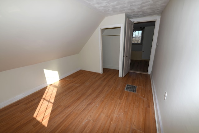 bonus room featuring light wood-type flooring, a textured ceiling, and vaulted ceiling