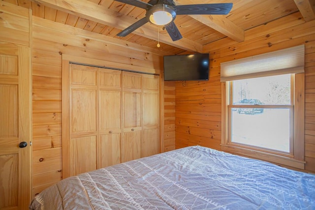 bedroom featuring wooden walls, ceiling fan, beamed ceiling, wood ceiling, and a closet