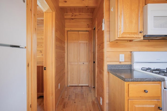 kitchen with light hardwood / wood-style floors, wood walls, white appliances, and beamed ceiling