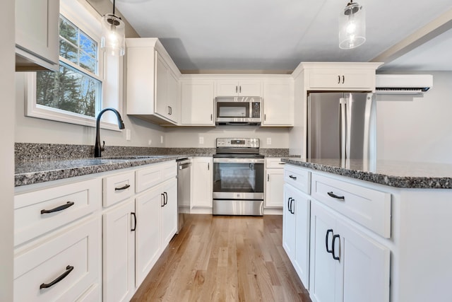 kitchen featuring decorative light fixtures, light hardwood / wood-style floors, white cabinetry, and appliances with stainless steel finishes