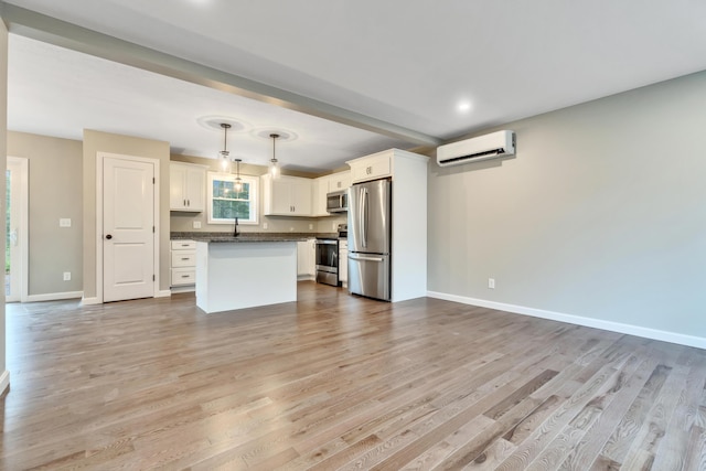 kitchen featuring a wall mounted air conditioner, hanging light fixtures, appliances with stainless steel finishes, a kitchen island, and white cabinetry