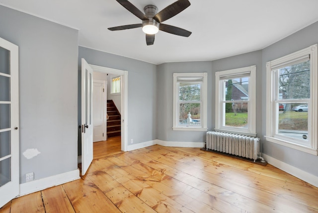 unfurnished room with radiator heating unit, light wood-type flooring, and ceiling fan