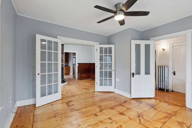 empty room with ceiling fan, french doors, light hardwood / wood-style flooring, and radiator heating unit