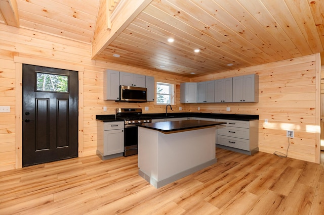 kitchen featuring appliances with stainless steel finishes, light wood-type flooring, gray cabinets, a kitchen island, and wooden walls