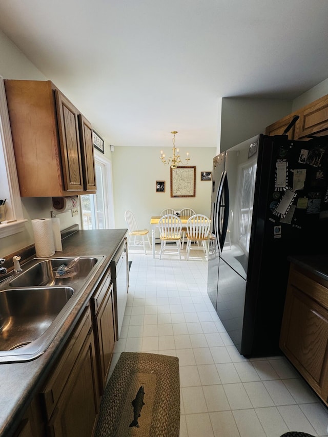 kitchen featuring an inviting chandelier, freestanding refrigerator, a sink, dishwasher, and dark countertops