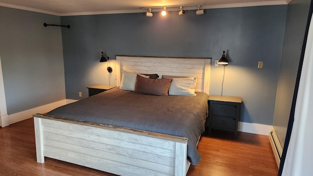 bedroom featuring track lighting, baseboard heating, hardwood / wood-style flooring, and crown molding