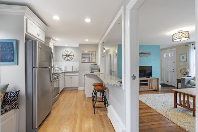 kitchen featuring a kitchen bar, light stone countertops, stainless steel appliances, white cabinets, and light hardwood / wood-style floors