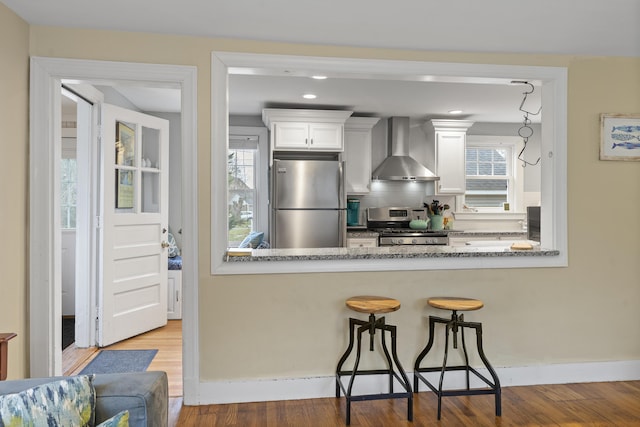 kitchen featuring hardwood / wood-style floors, stainless steel appliances, white cabinetry, and wall chimney range hood