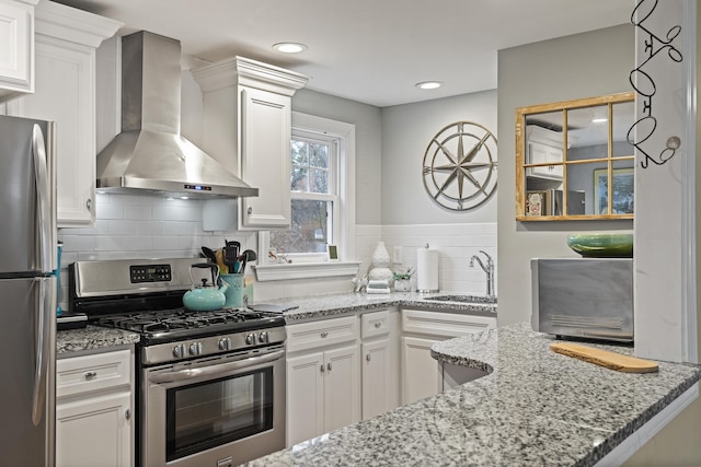 kitchen featuring white cabinets, wall chimney range hood, sink, light stone counters, and stainless steel appliances