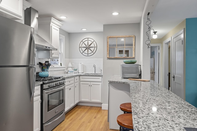 kitchen with white cabinets, appliances with stainless steel finishes, light wood-type flooring, and wall chimney range hood