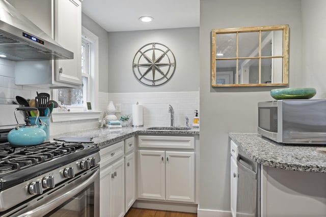 kitchen featuring decorative backsplash, appliances with stainless steel finishes, wall chimney exhaust hood, sink, and white cabinets