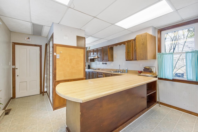 kitchen featuring a drop ceiling, light tile patterned flooring, kitchen peninsula, and sink