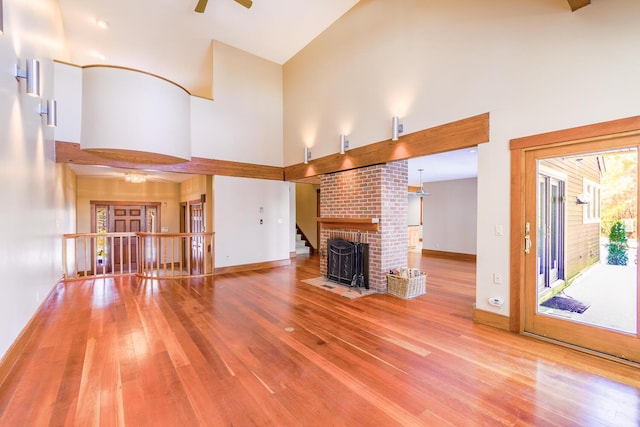 unfurnished living room with a brick fireplace, high vaulted ceiling, and hardwood / wood-style flooring