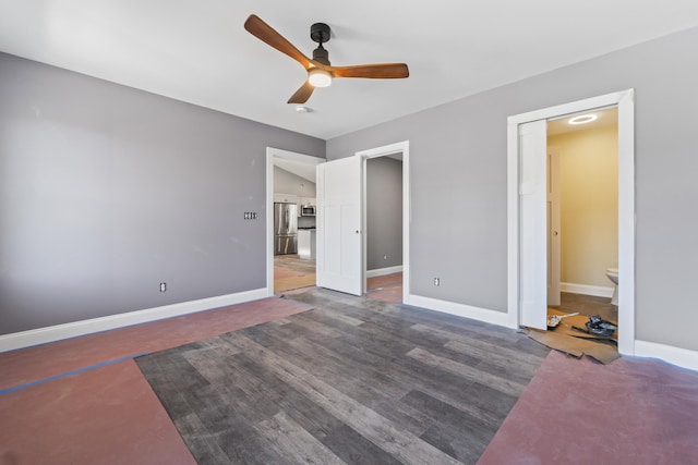 unfurnished bedroom with stainless steel fridge, connected bathroom, ceiling fan, and dark wood-type flooring