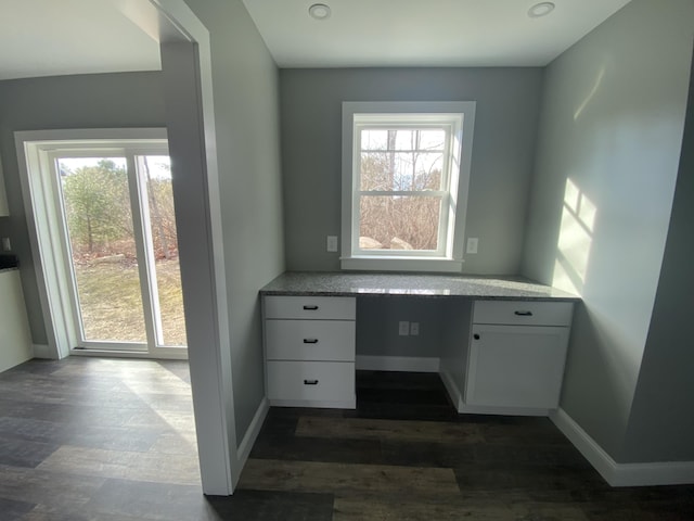 unfurnished office with dark hardwood / wood-style flooring, built in desk, and a wealth of natural light