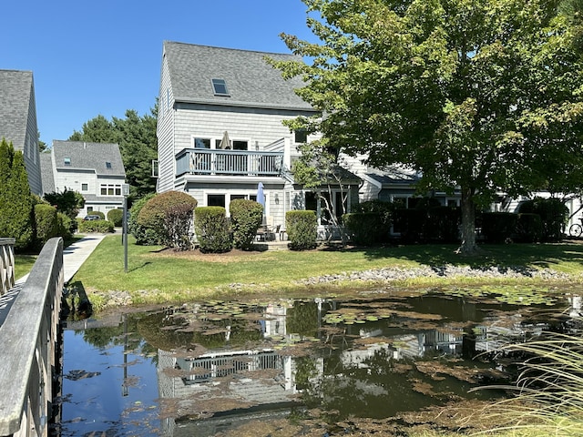 rear view of property with a yard, a balcony, and a water view