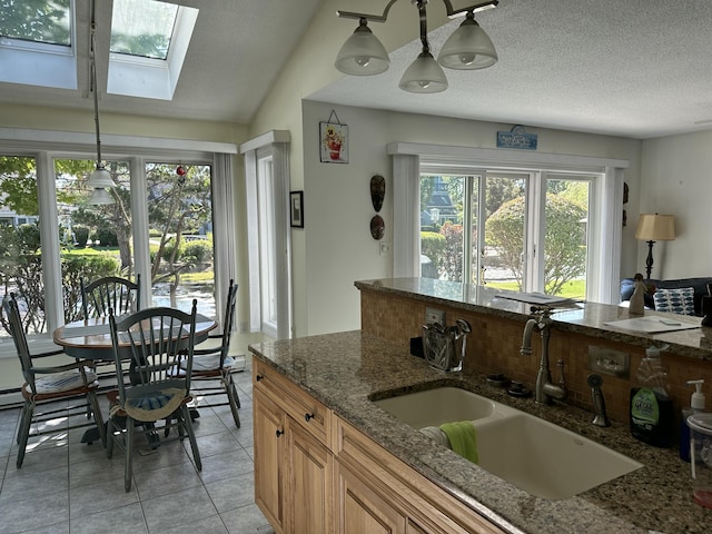 kitchen featuring sink, vaulted ceiling with skylight, dark stone countertops, a textured ceiling, and decorative light fixtures