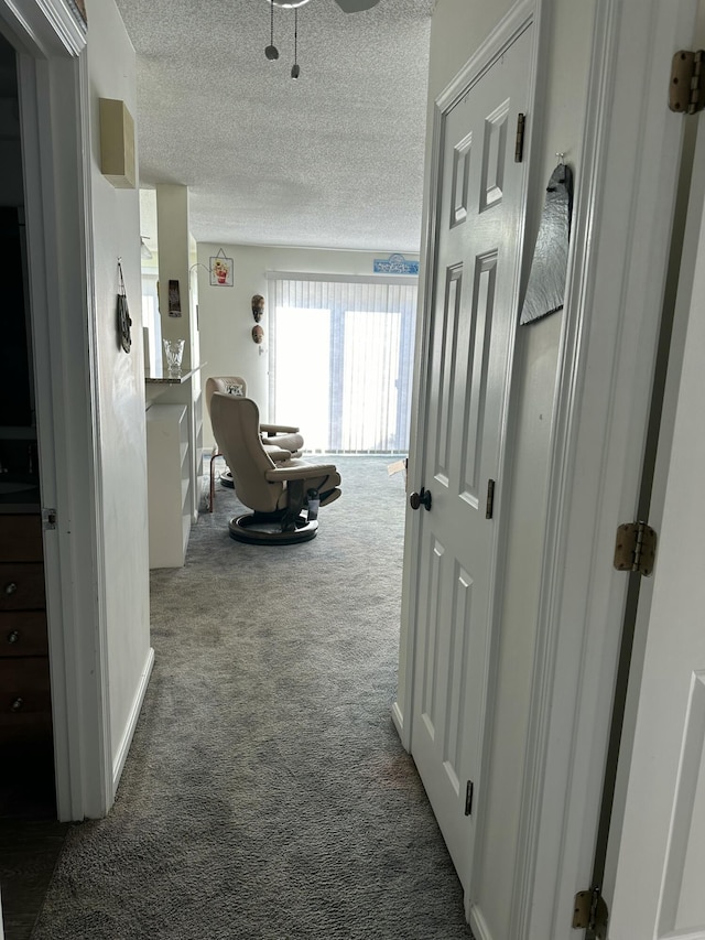 hallway with a textured ceiling and dark colored carpet