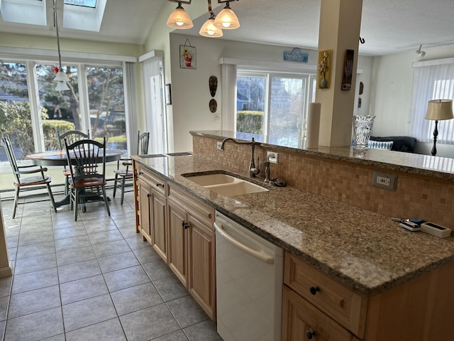 kitchen with pendant lighting, sink, a skylight, stainless steel dishwasher, and tasteful backsplash