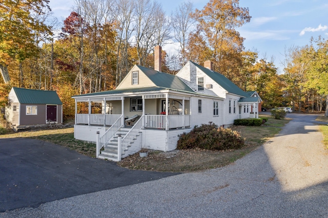 view of front of home featuring a chimney, metal roof, an outbuilding, a storage unit, and a porch