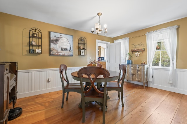 dining area featuring a wainscoted wall, a notable chandelier, and light wood-style floors