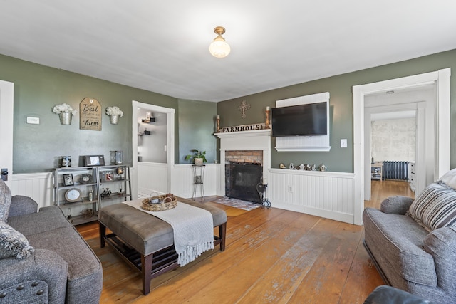 living room with hardwood / wood-style floors, radiator heating unit, wainscoting, and a brick fireplace