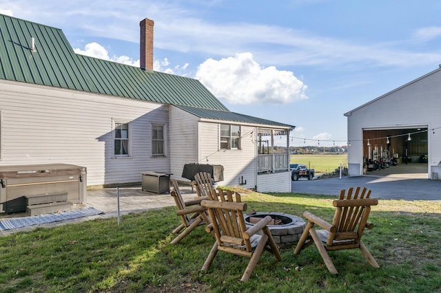 rear view of property with an outdoor fire pit, a hot tub, a chimney, metal roof, and a yard