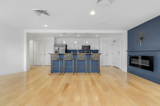 kitchen featuring appliances with stainless steel finishes, a kitchen breakfast bar, light hardwood / wood-style flooring, white cabinets, and hanging light fixtures