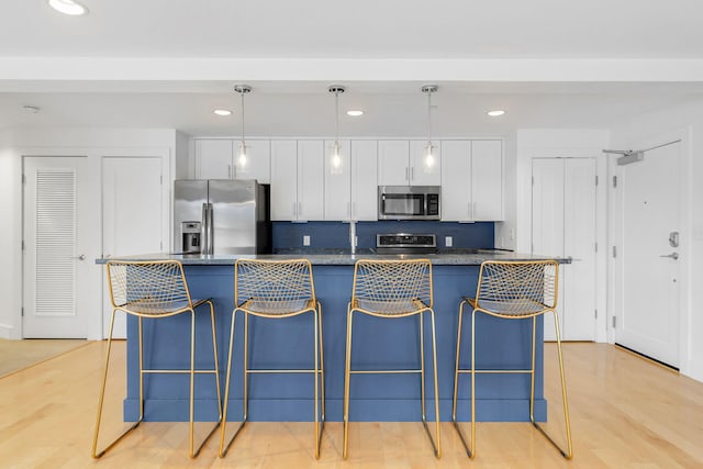 kitchen featuring white cabinets, hanging light fixtures, light hardwood / wood-style flooring, a kitchen island, and stainless steel appliances