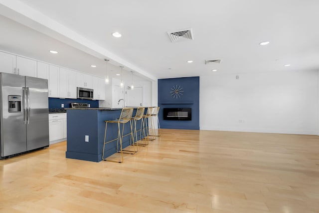 kitchen with appliances with stainless steel finishes, decorative light fixtures, a center island with sink, light hardwood / wood-style flooring, and white cabinetry