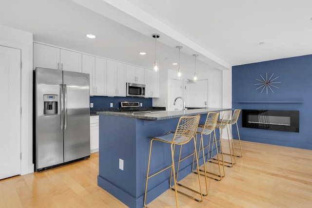 kitchen featuring appliances with stainless steel finishes, a kitchen island with sink, light hardwood / wood-style flooring, white cabinets, and hanging light fixtures