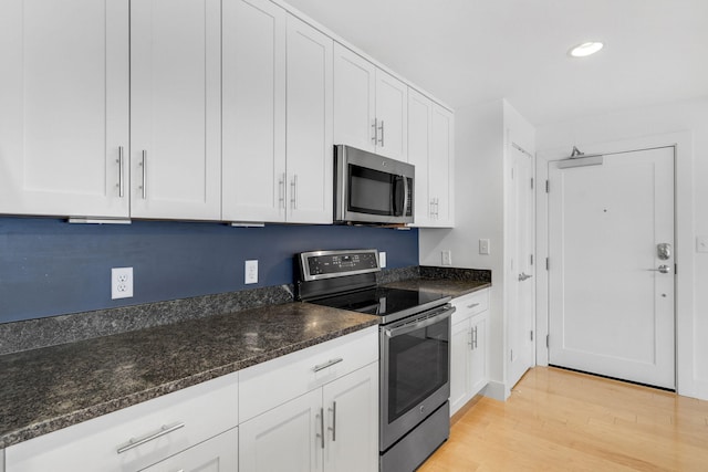 kitchen with dark stone counters, white cabinets, stainless steel appliances, and light hardwood / wood-style floors