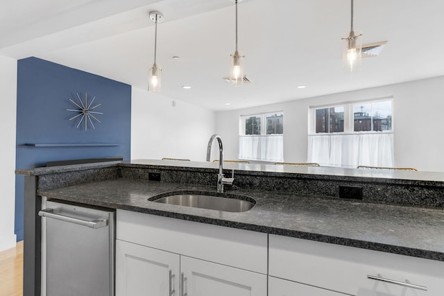 kitchen with pendant lighting, dark stone counters, white cabinets, sink, and light wood-type flooring